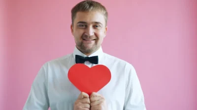 Man in white shirt holding red heart on pink background