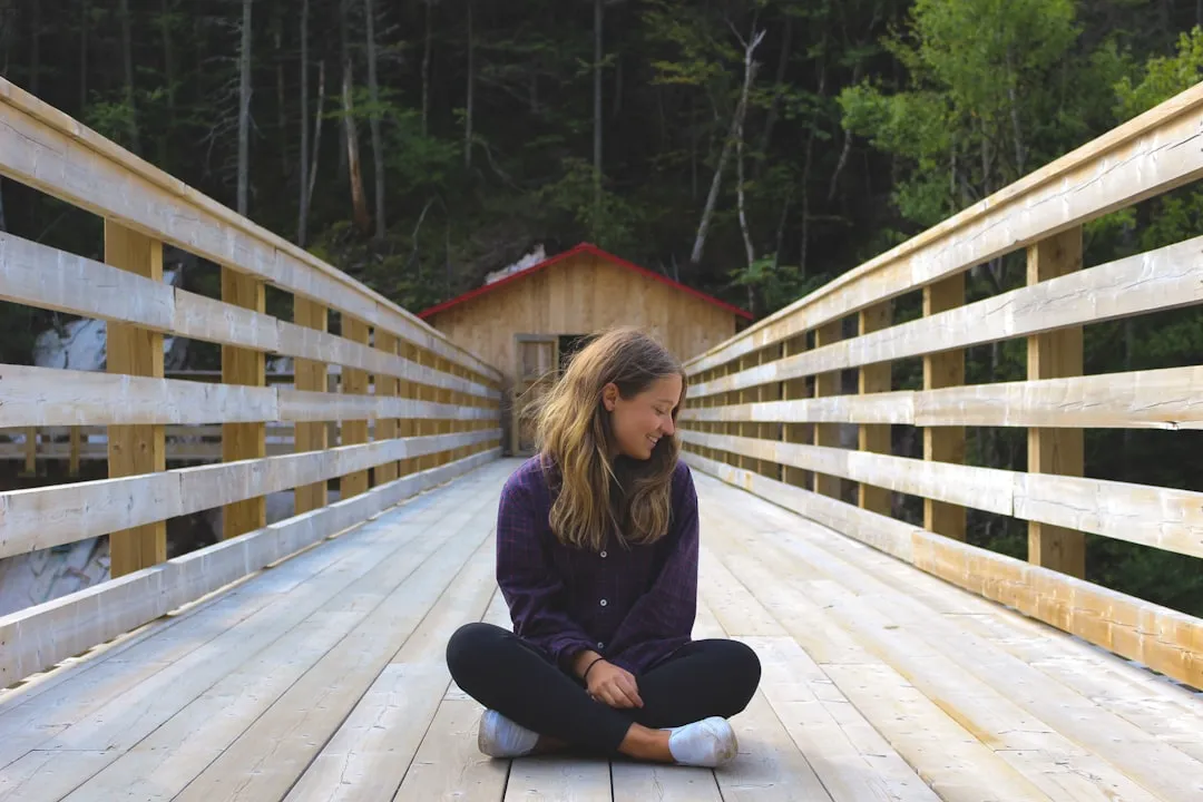 woman sitting on wooden bridge near forest