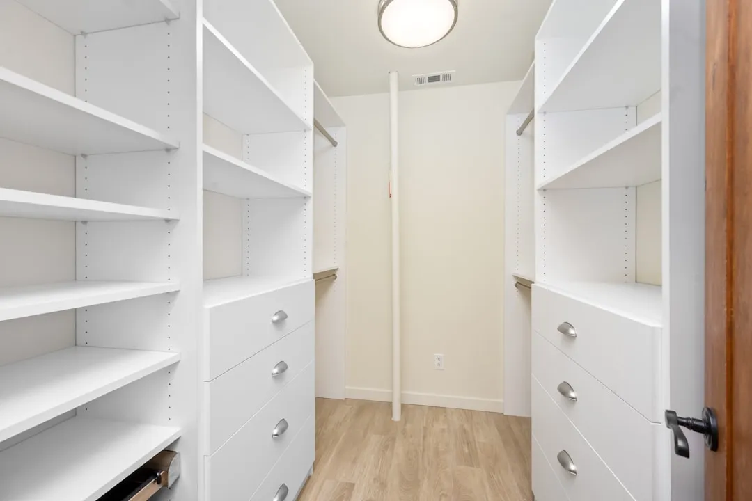 A walk in closet with white shelves and drawers