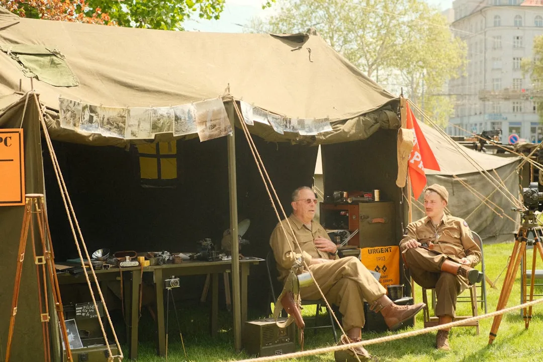Two people in uniforms sit outside of a tent.
