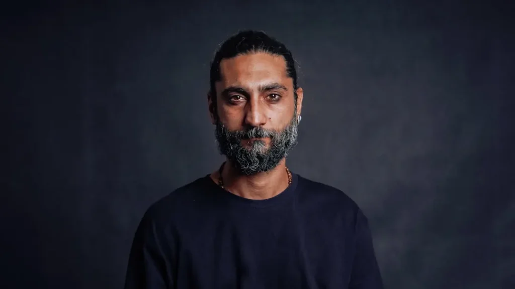 A man stares at the camera, against a dark backdrop.