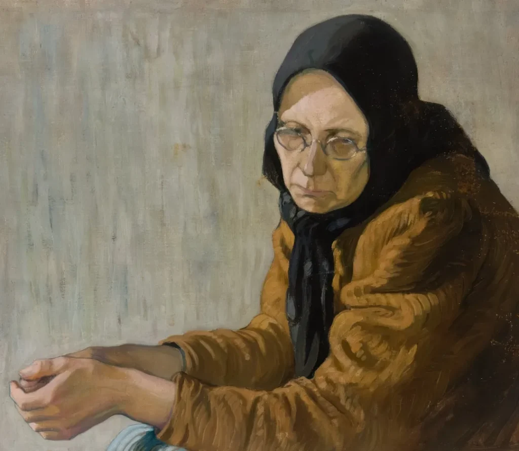 An elderly woman in glasses and headscarf looks thoughtfully.