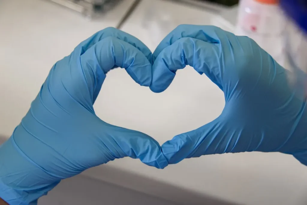 Hands in gloves forming a heart shape.