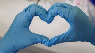 Hands in gloves forming a heart shape.