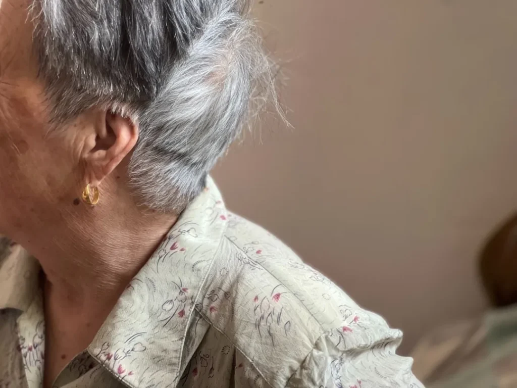 An elderly woman with grey hair and jewelry.