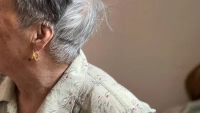 An elderly woman with grey hair and jewelry.