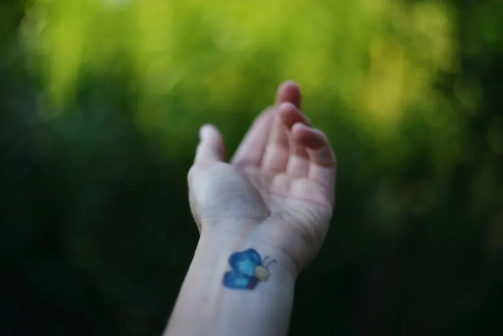 A hand displays a blue butterfly tattoo.