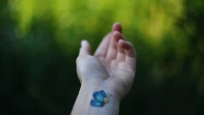 A hand displays a blue butterfly tattoo.