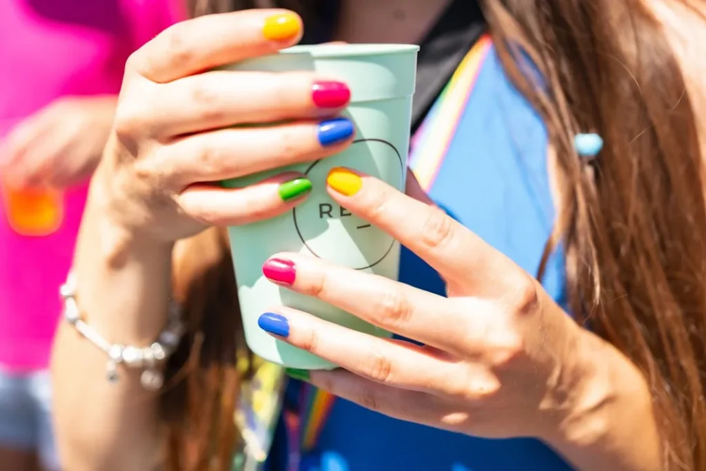 Woman's hands holding a cup with rainbow-colored nails.