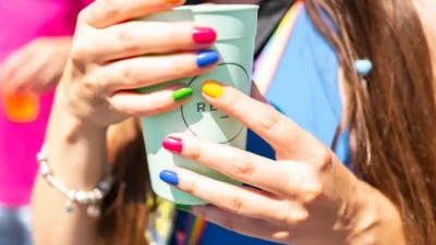 Woman's hands holding a cup with rainbow-colored nails.