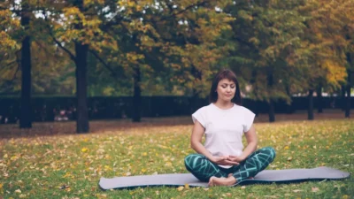 Woman meditating peacefully on yoga mat in autumn park.