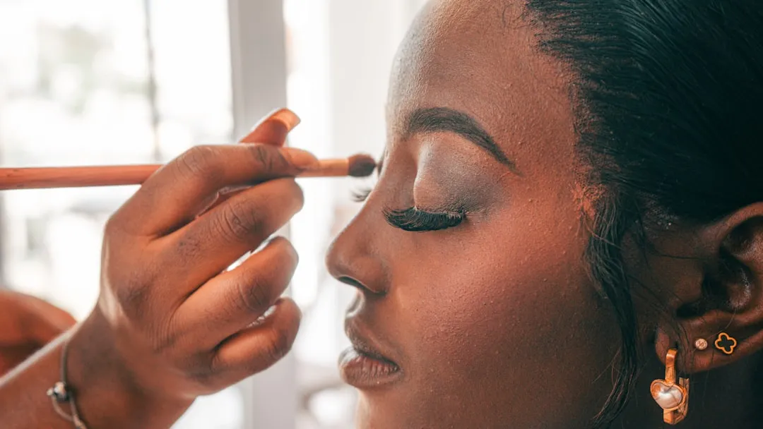 A makeup artist applies eyeshadow to a woman's eyelid.