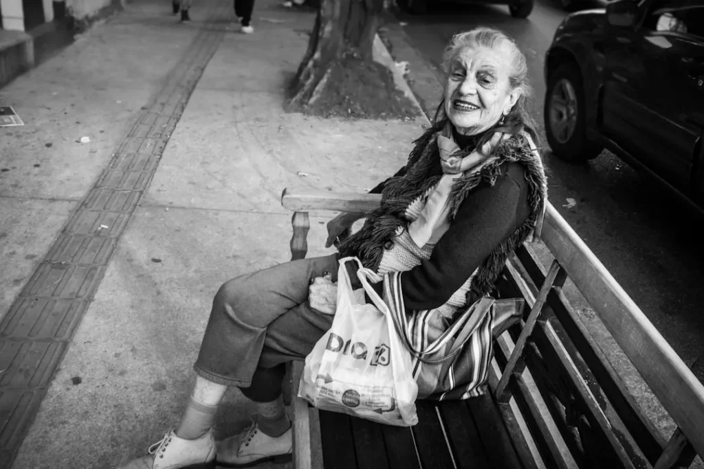 Elderly woman smiles while sitting on a park bench.