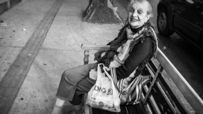 Elderly woman smiles while sitting on a park bench.