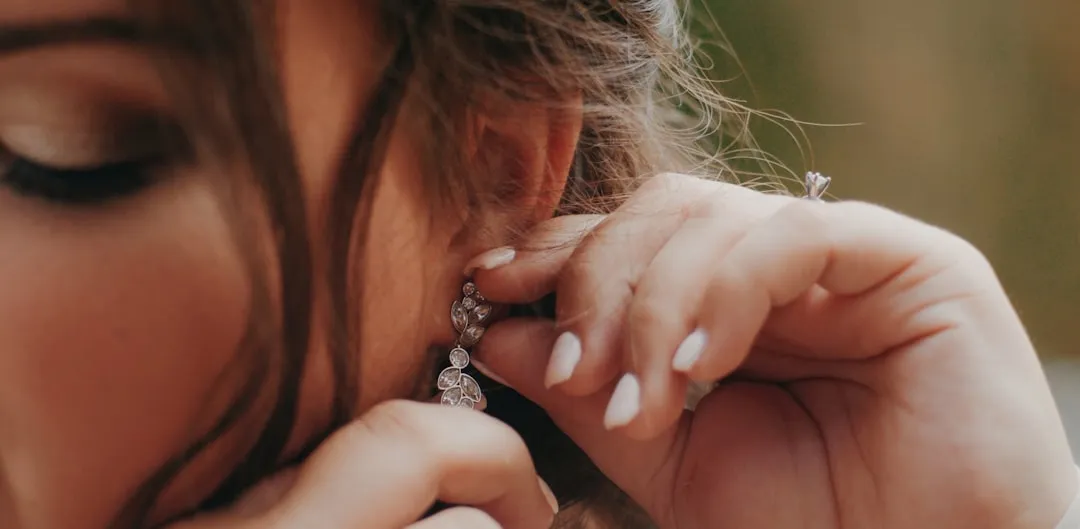 a close up of a person putting on a pair of earrings