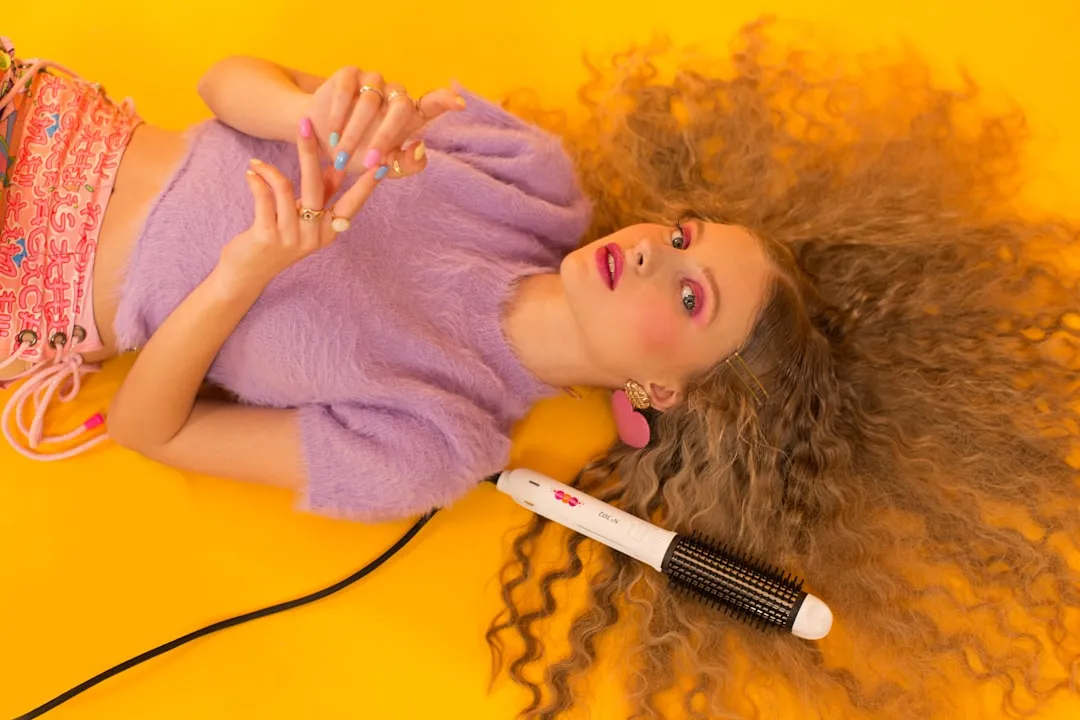 Woman with voluminous curly hair and styling tool on yellow.
